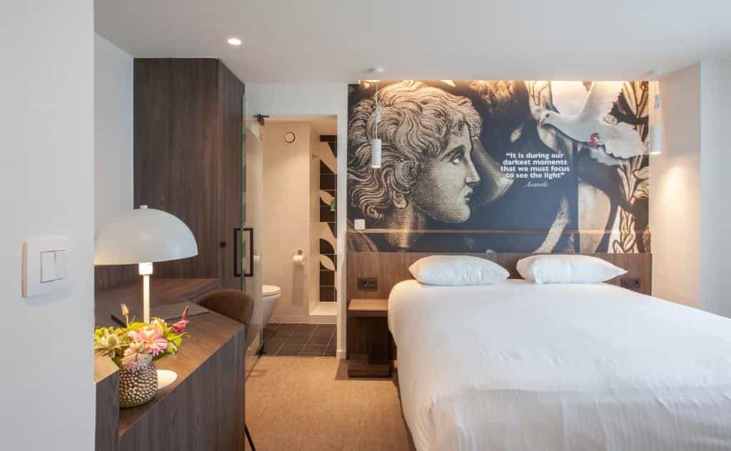 Hotel room with white bedding, desk, and wall art featuring a classical profile and a dove.