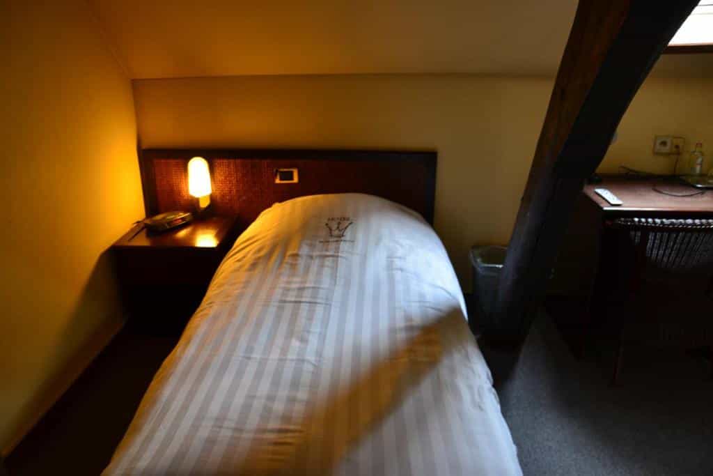 Single bed with striped duvet in dimly lit hotel room with wooden beam structure.