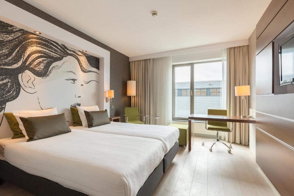 Twin hotel room with large graphic headboard mural, white bedding, and desk area.
