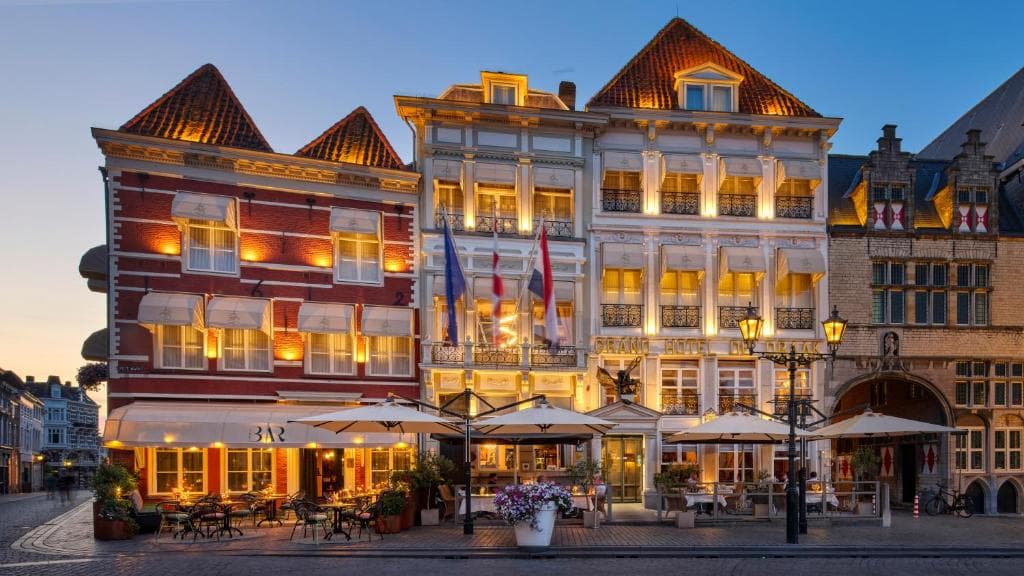 Historic European buildings with illuminated windows and outdoor cafe seating at dusk.