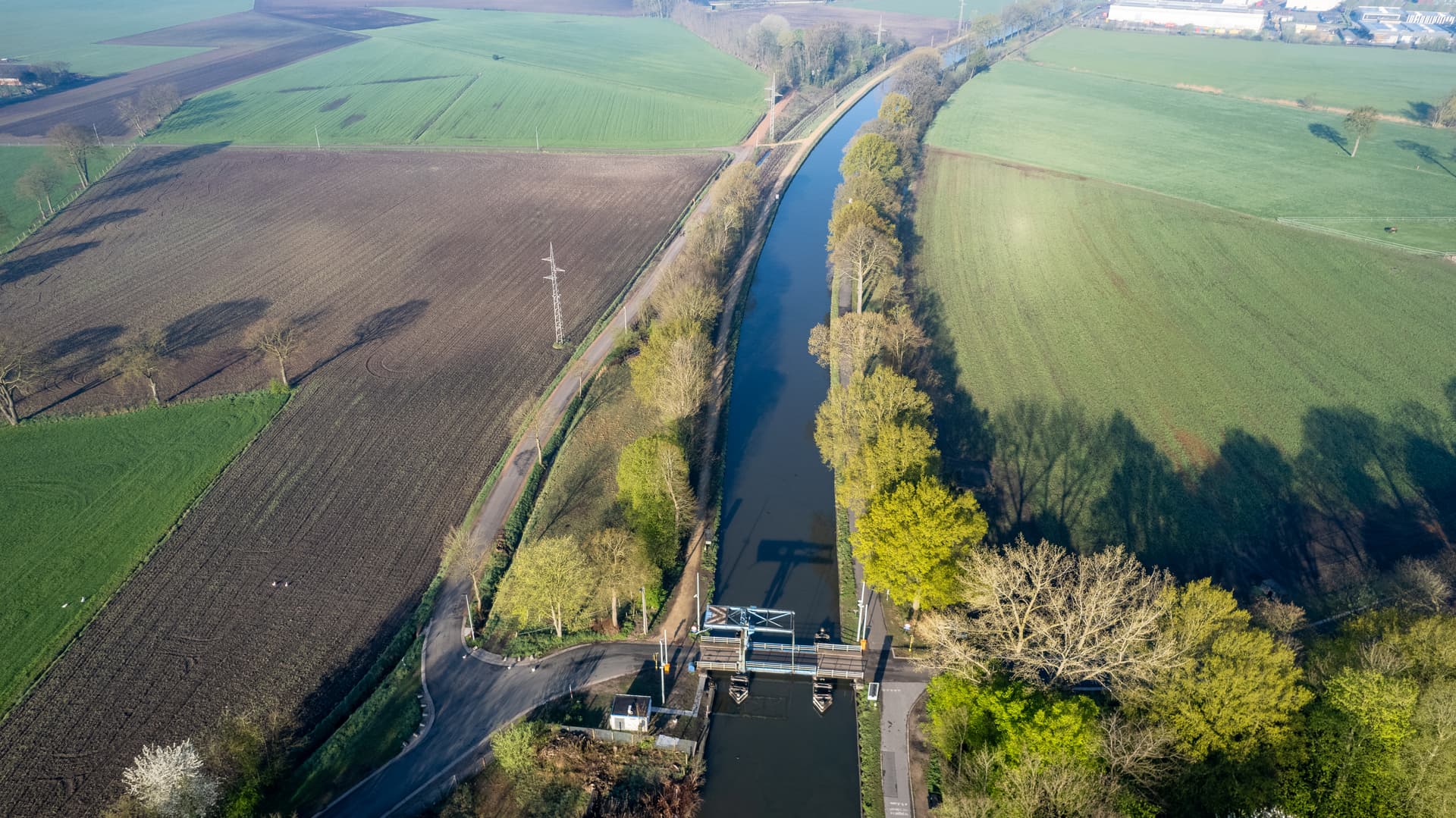Aerial view of a canal lock structure between green fields and plowed brown earth in Dessel-Schoten.