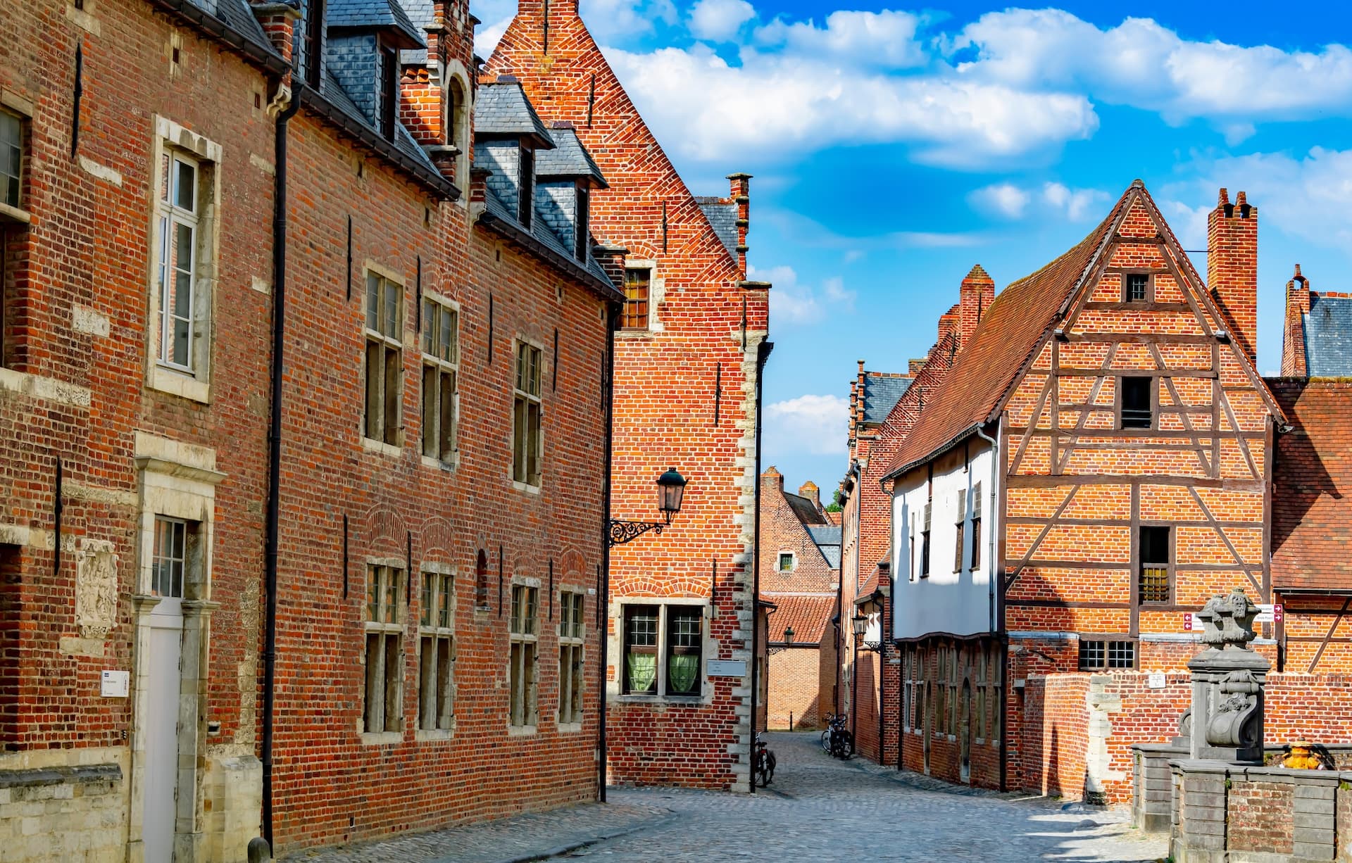 Cobblestone street lined with historic brick and timber-framed buildings under a blue sky in the Groot Begijnhof.