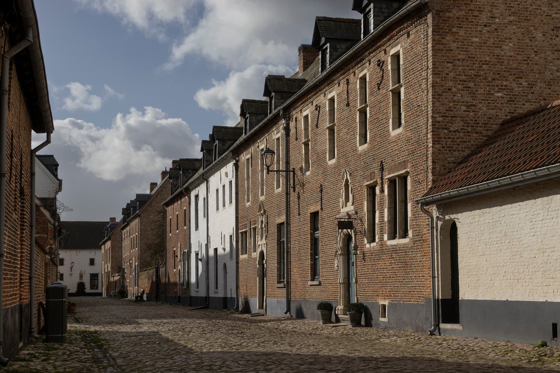 Cobblestone street lined with historic brick and white buildings under a cloudy sky in Diest.