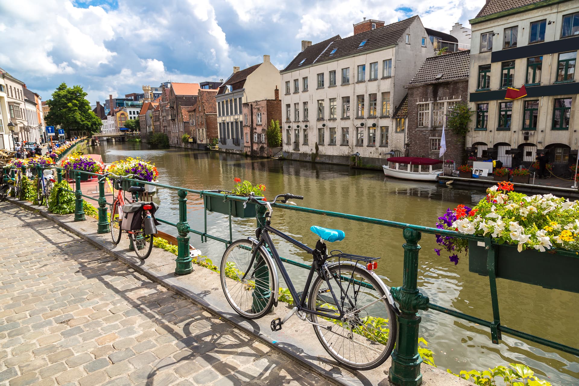 Bicycle parked by canal with historic buildings and flower boxes under blue sky