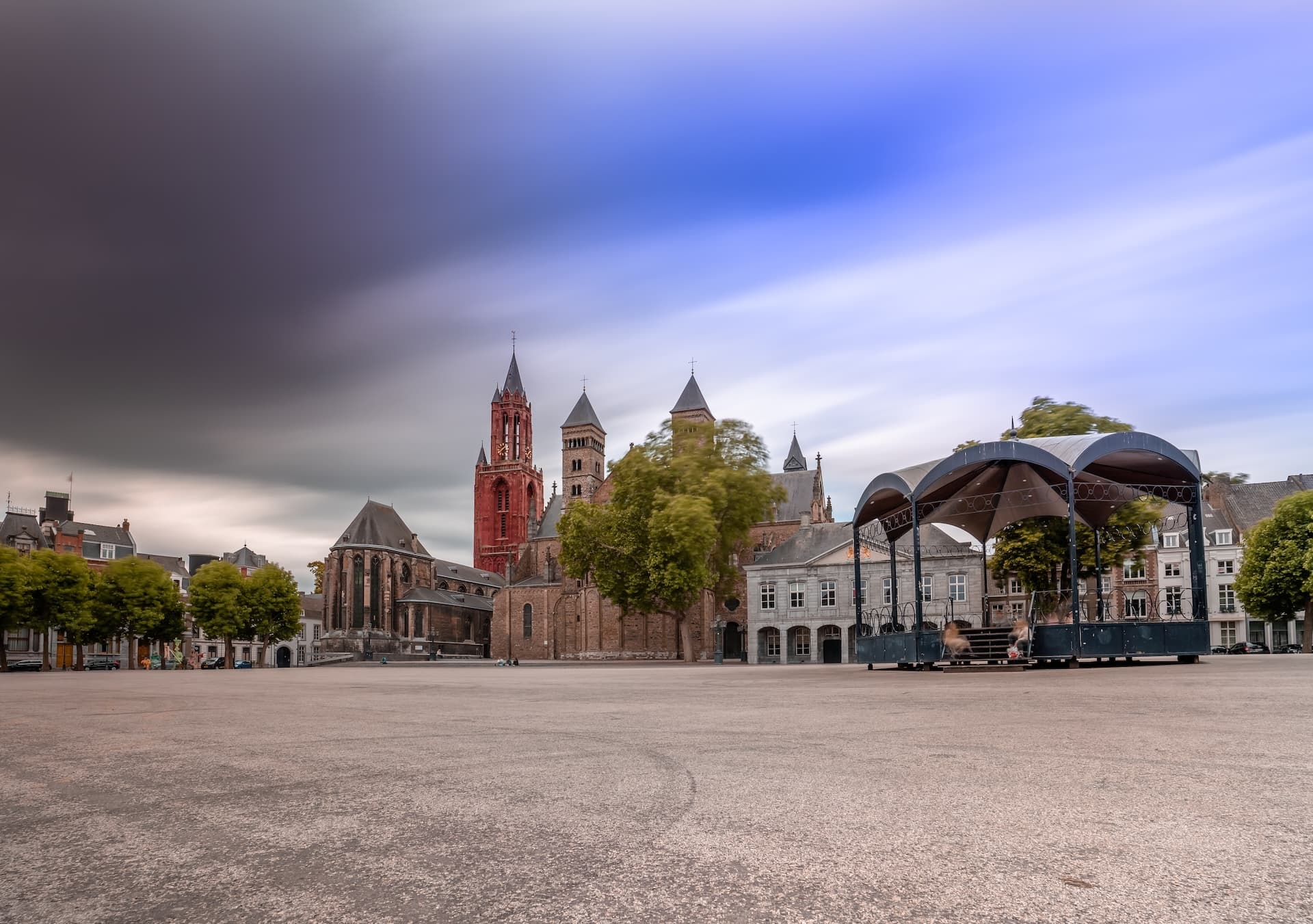 Vrijthof square with St Servatius Basilica and outdoor stage under dramatic, streaked sky.