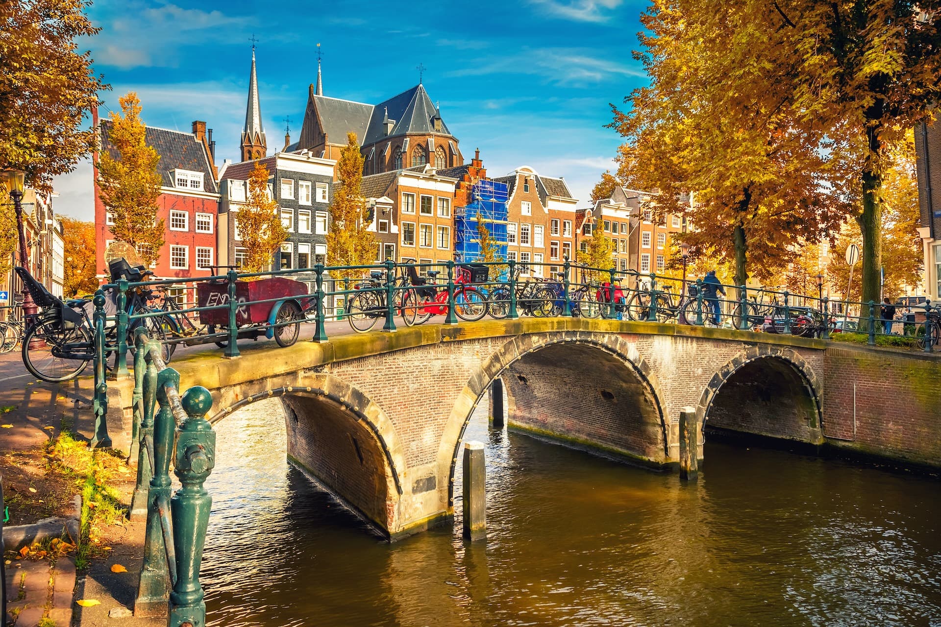 Brick arch bridge over canal with bicycles and autumn trees in Amsterdam