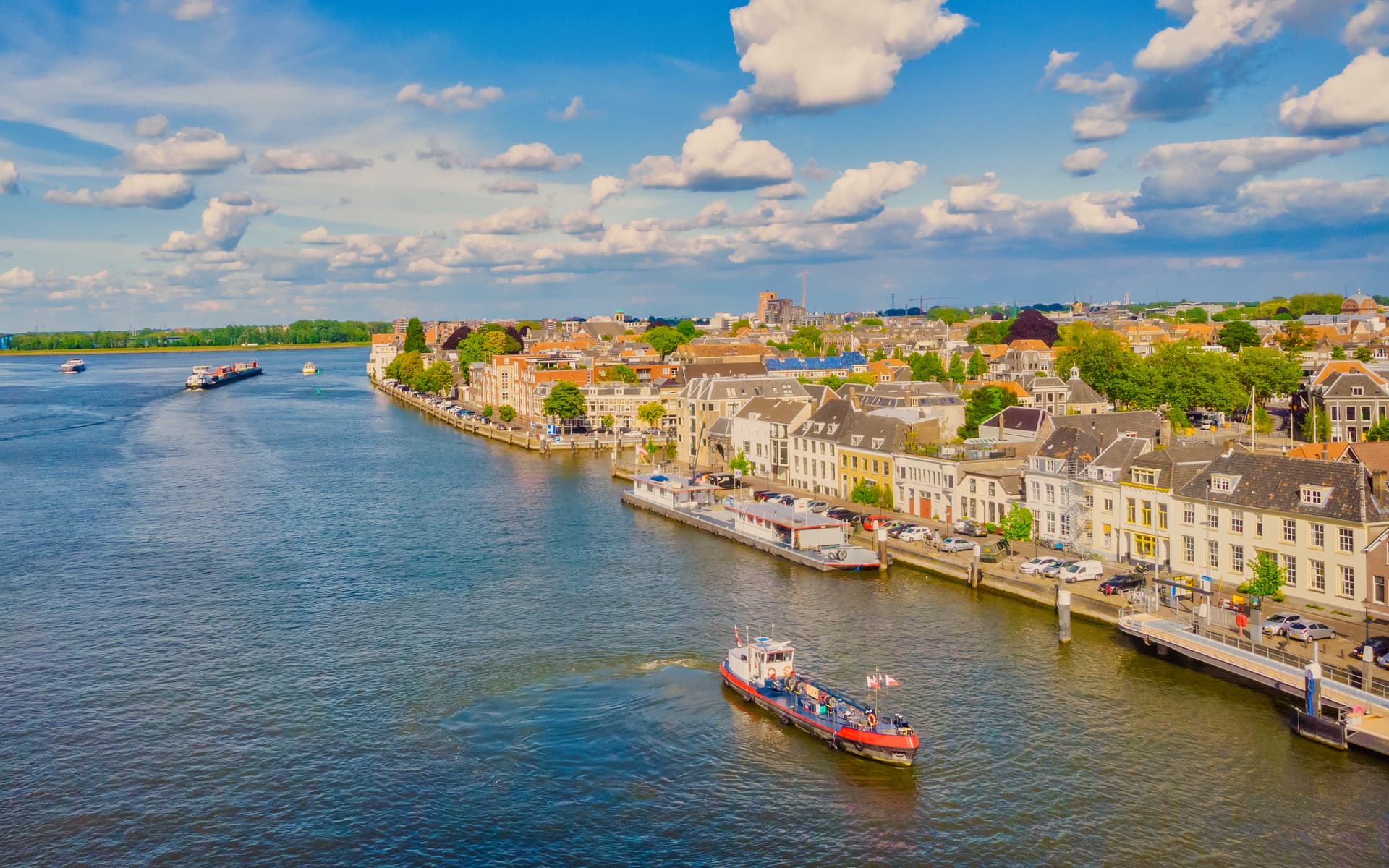 Small working boat on river next to historic buildings in Dordrecht under blue sky.