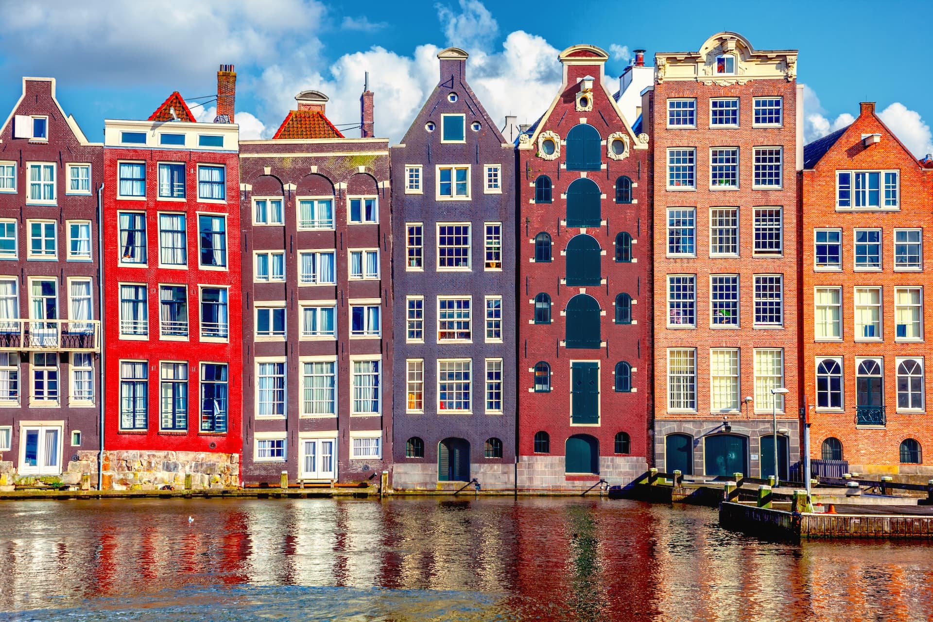 Colorful historic canal houses reflected in the water under a blue, cloudy sky.