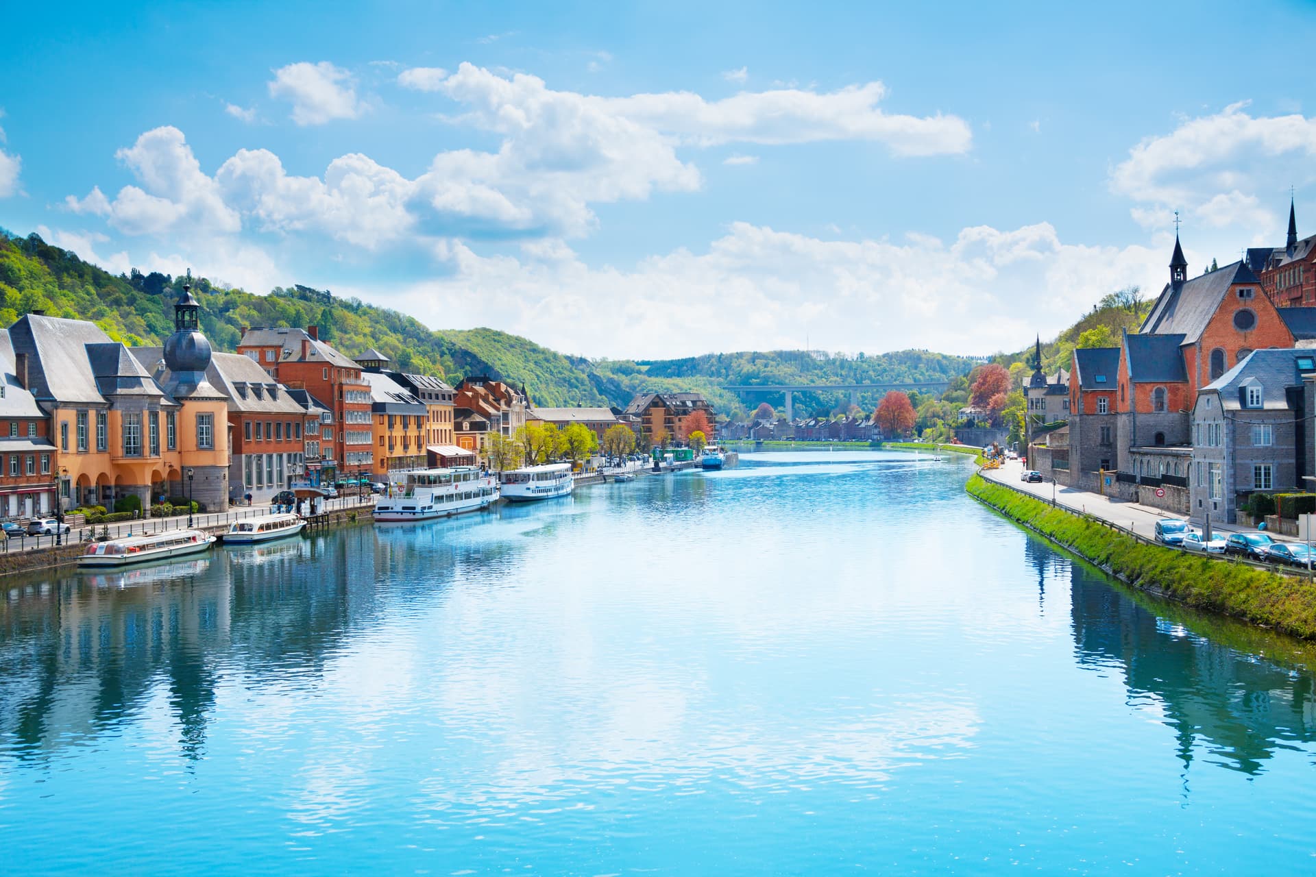 River cruise boats docked by historic buildings nestled in green hills under a blue sky.