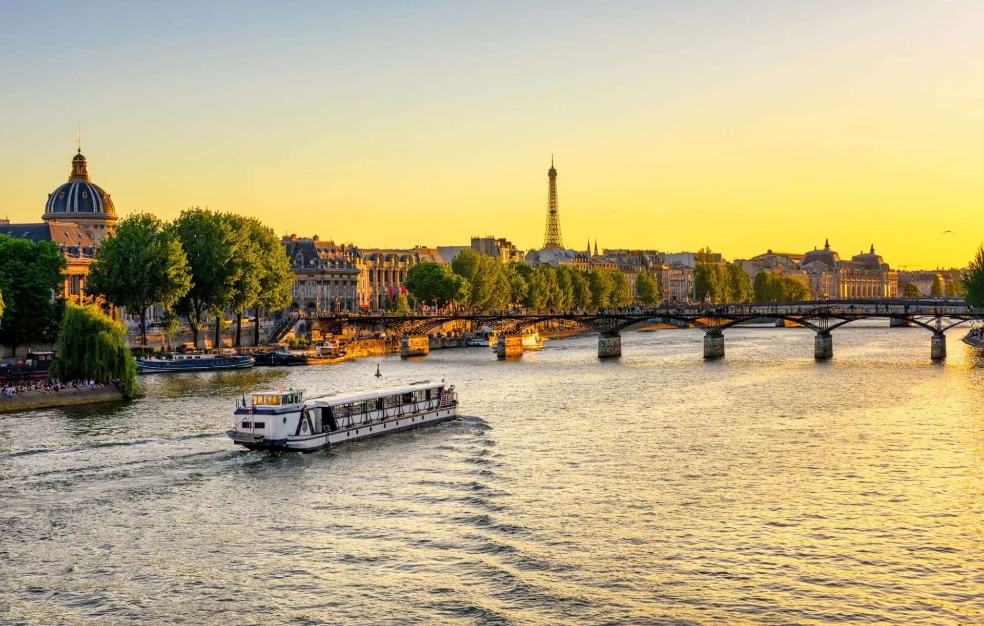 Tour boat on the Seine River in Paris at sunset with the Eiffel Tower visible.