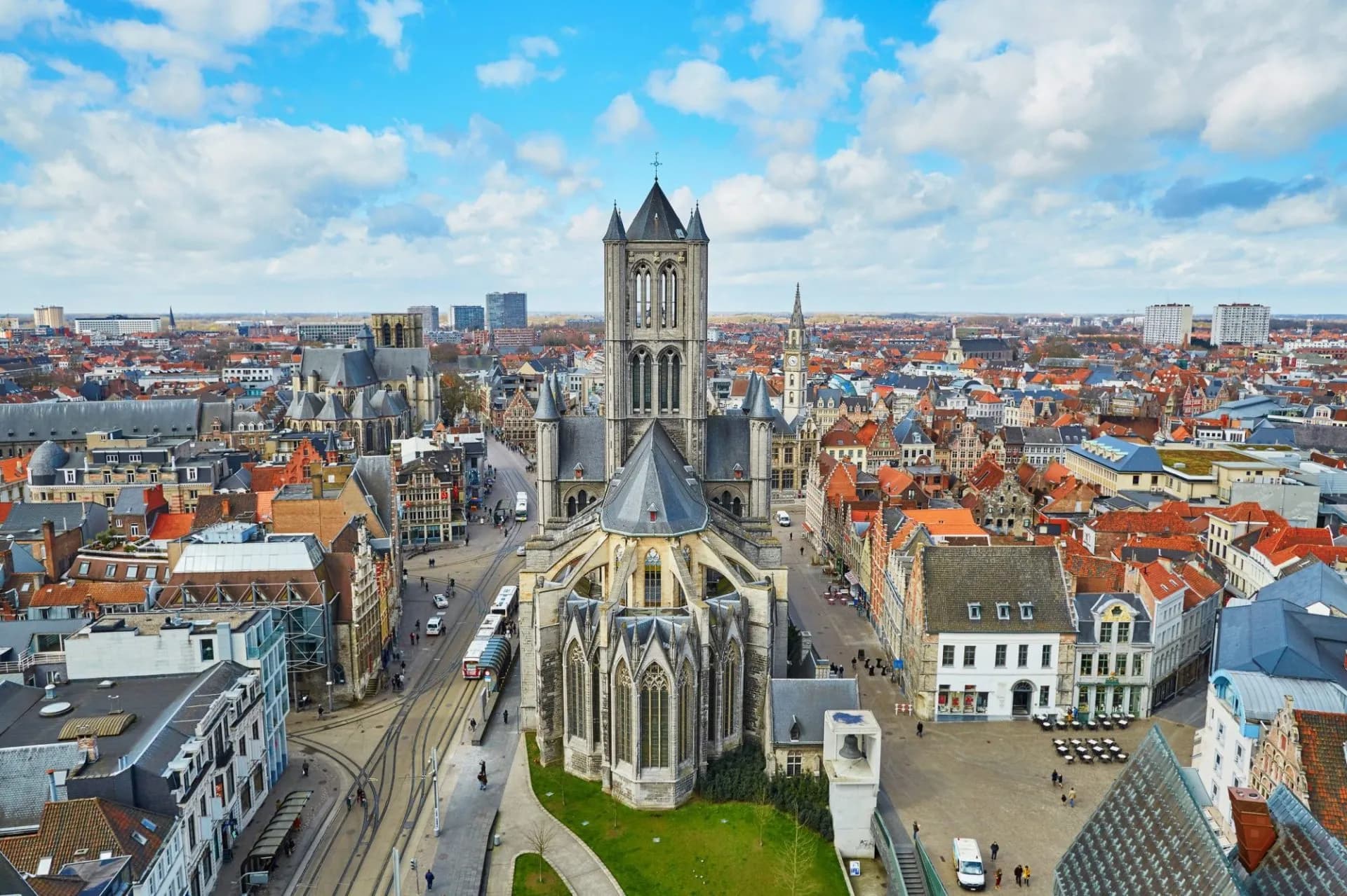 Ghent cityscape featuring St. Nicholas' Church tower over historic buildings and tram lines.