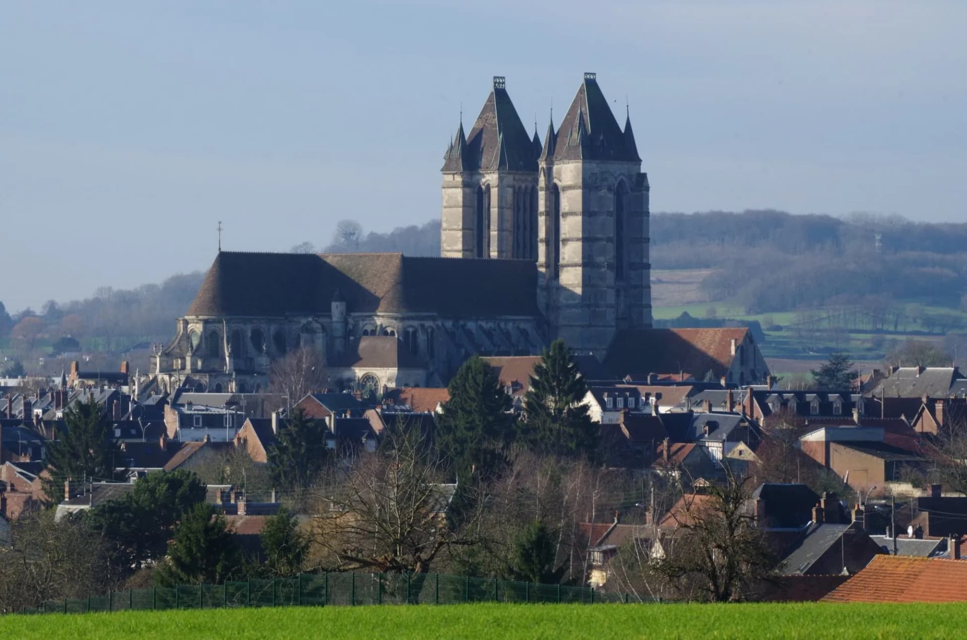 Large historic church with twin towers overlooking a town and rolling hills in Noyon.