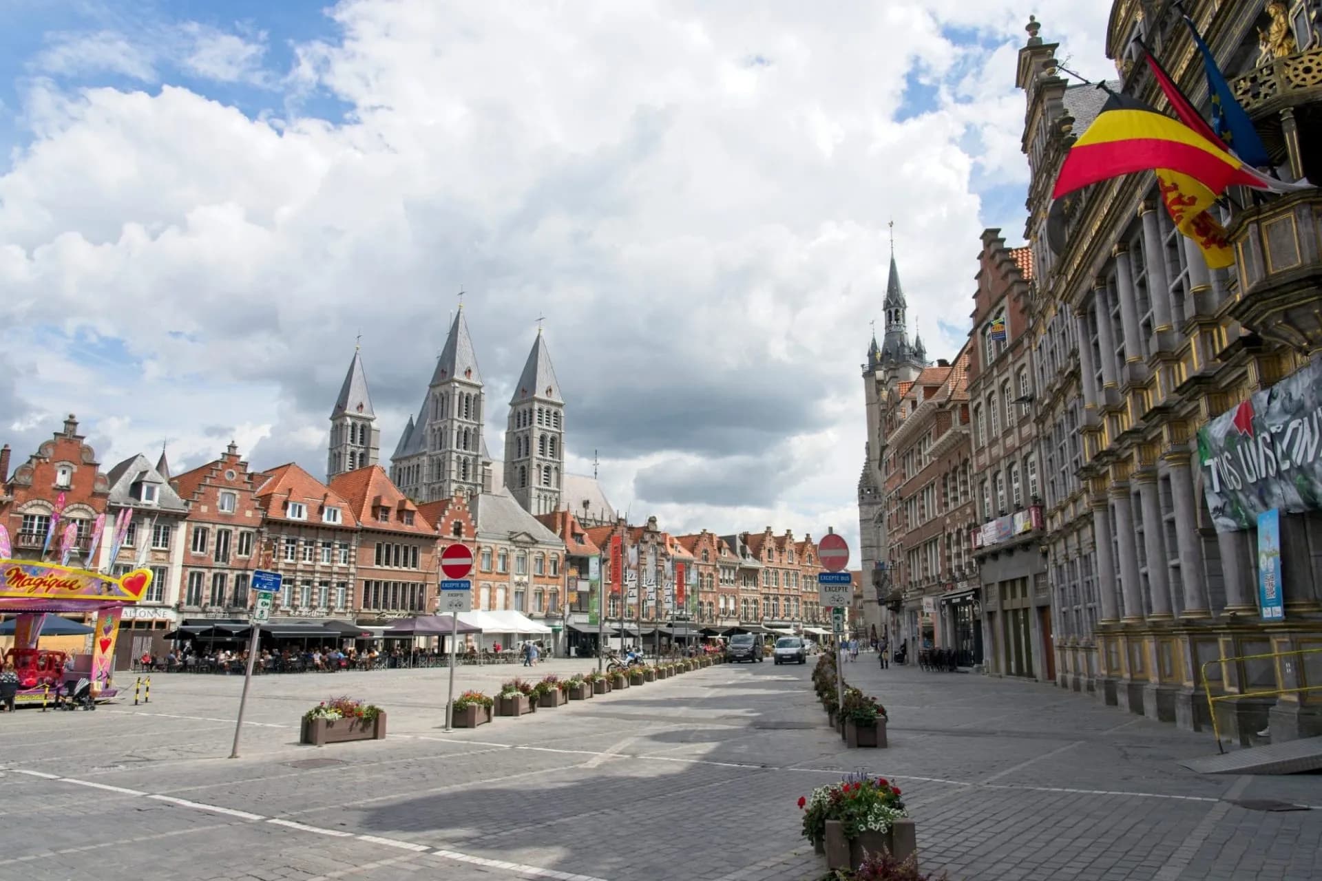 Cobblestone square in Tournai with historic buildings and cathedral towers under cloudy sky.