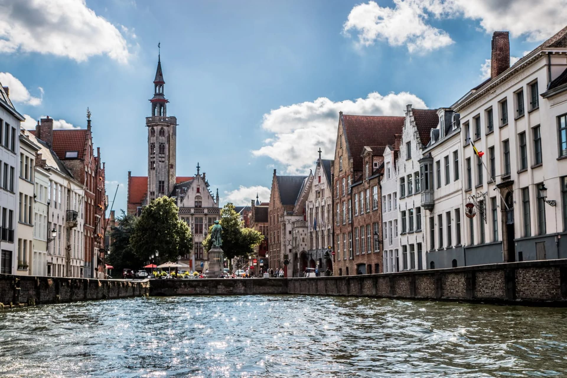 Canal du Nord with historic European buildings and a prominent tower under a blue, cloudy sky.