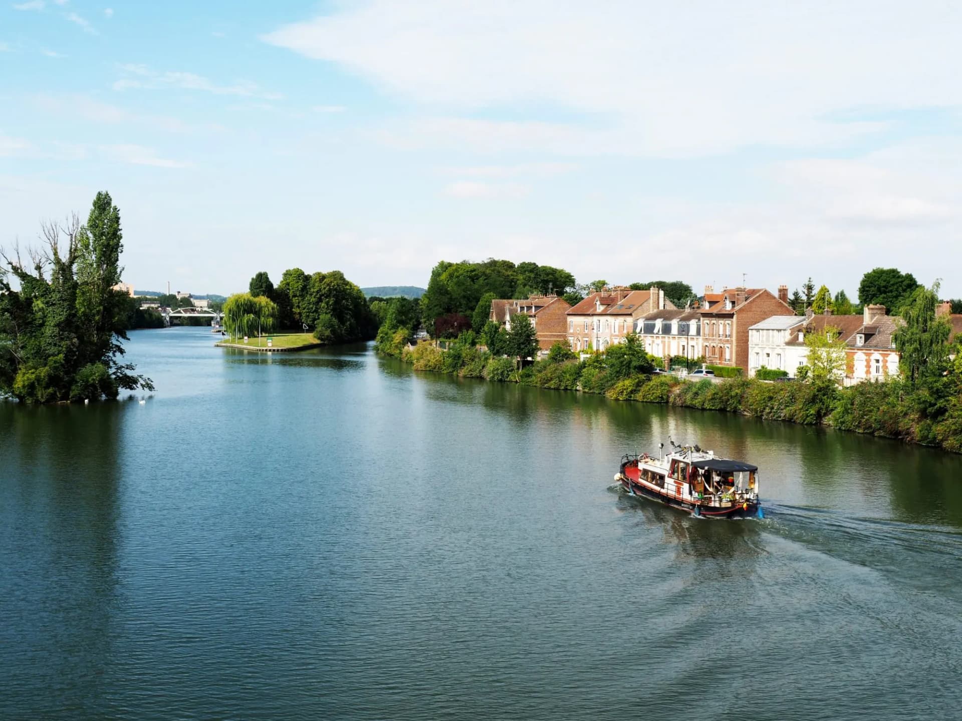Motorized boat cruising on river near town with brick houses, Compiègne.