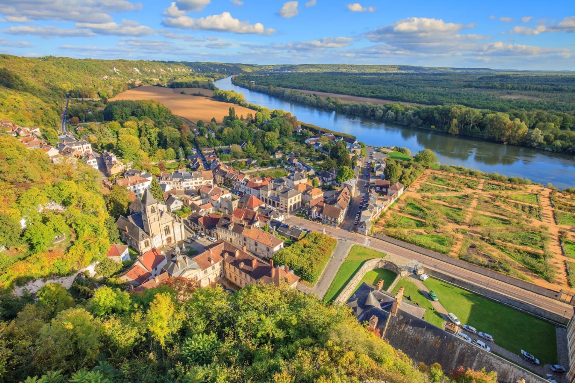 Aerial view of a town nestled by a wide river valley with autumn foliage.