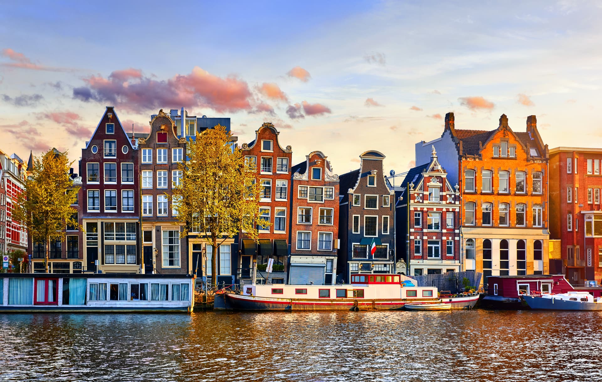 Houseboats moored along canal lined with historic brick buildings in Amsterdam at sunset.