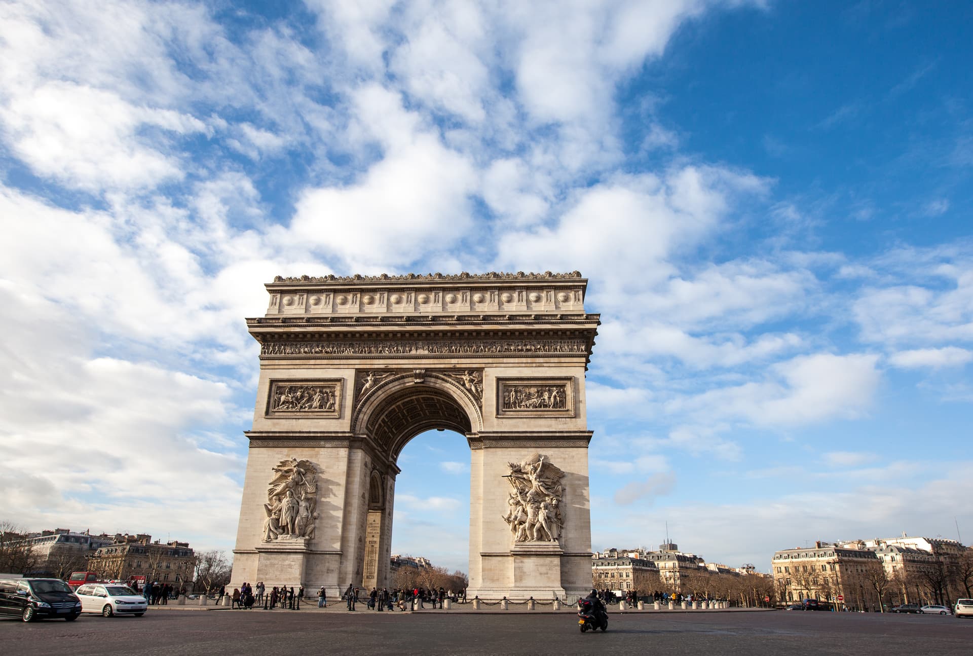 Arc de Triomphe monument in Paris under a blue sky with white clouds, with traffic below.
