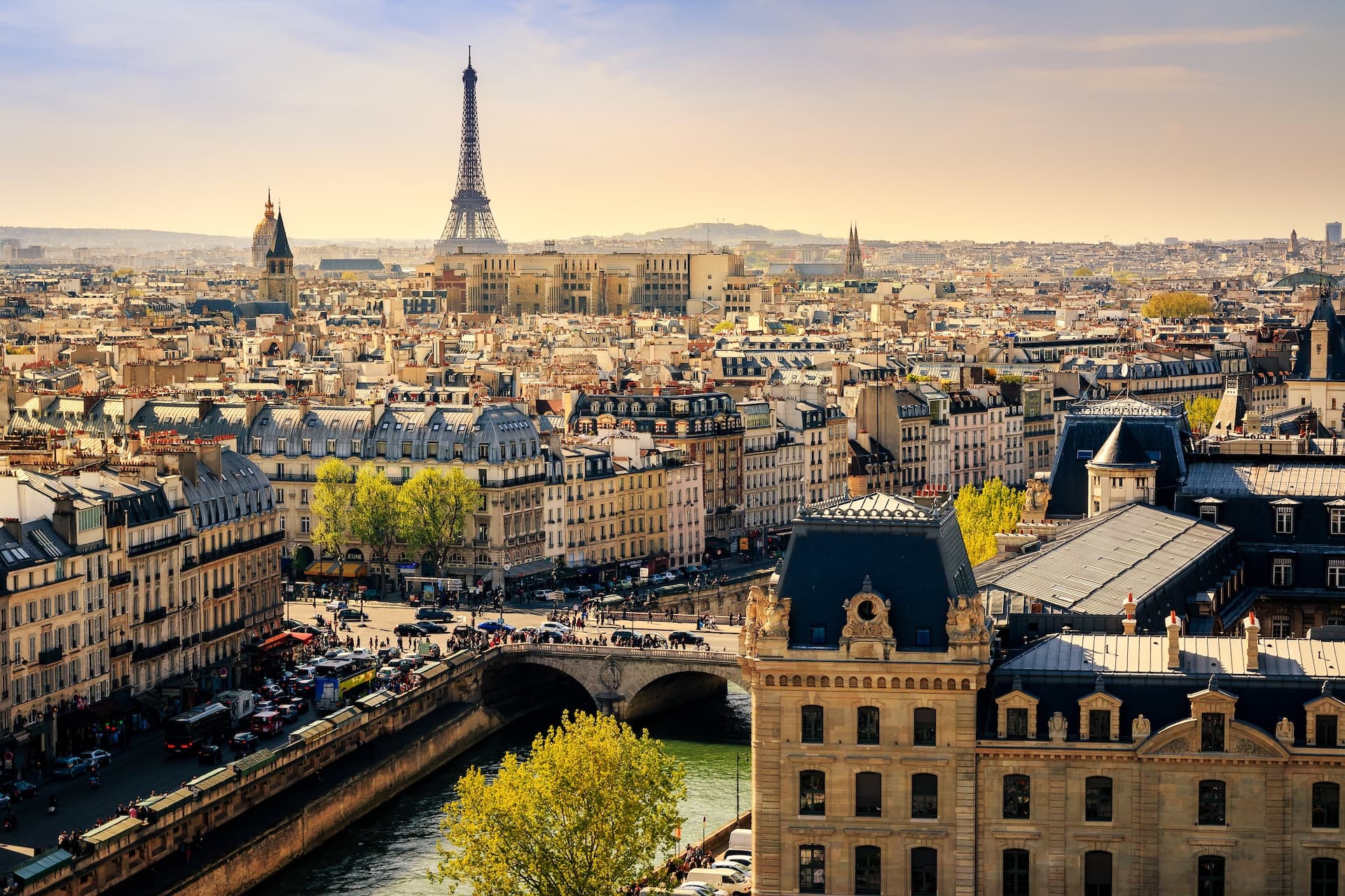 Paris cityscape with Eiffel Tower, river, bridge, and Haussmann-style buildings.