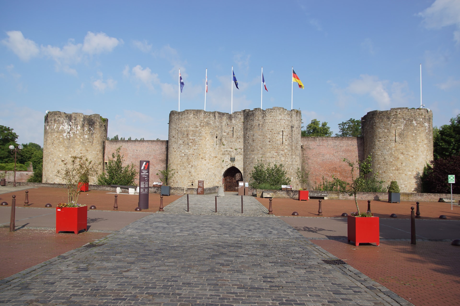 Stone fortress entrance with round towers, flags flying, and cobblestone square in Péronne.