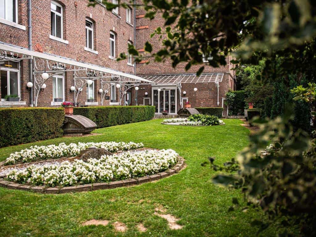 Manicured garden with white flowers and hedge in front of a brick building with glass awning.