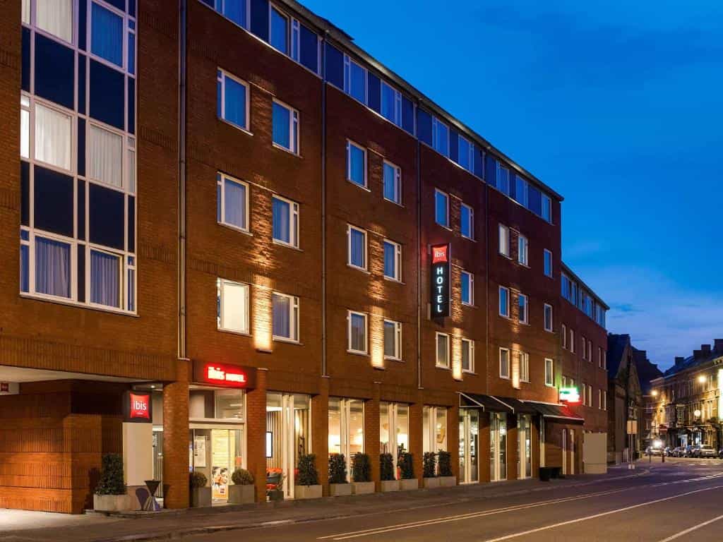 Ibis hotel exterior with illuminated signage on a brick building along a street at dusk.