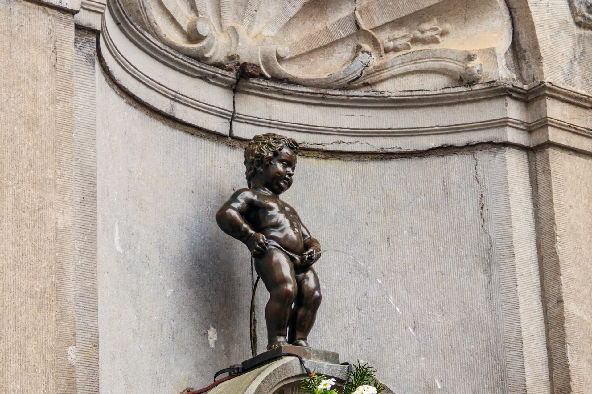 Manneken Pis bronze statue urinating against a textured stone wall in Brussels