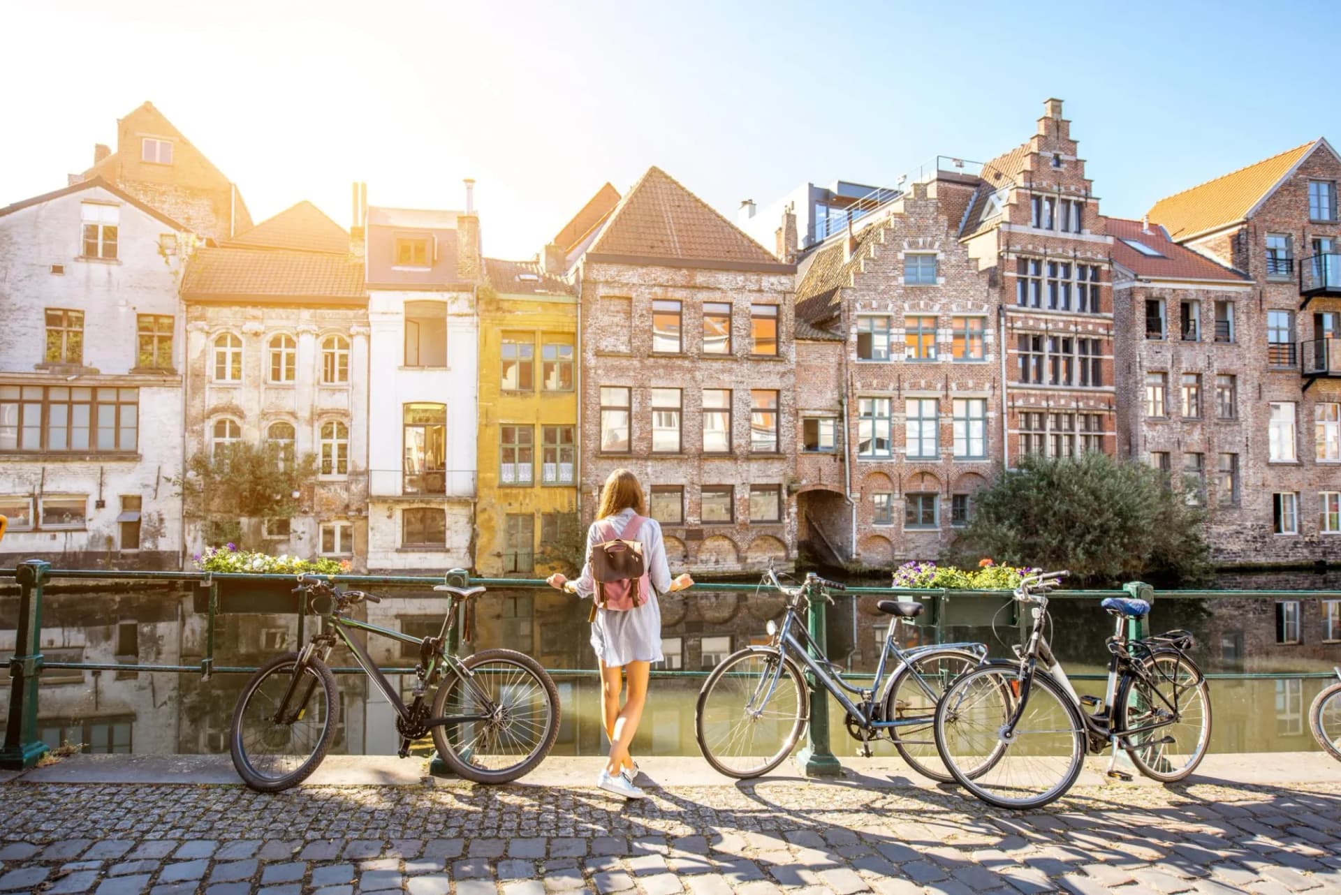 Woman with bicycles near water channel with old buildings in Ghent city.