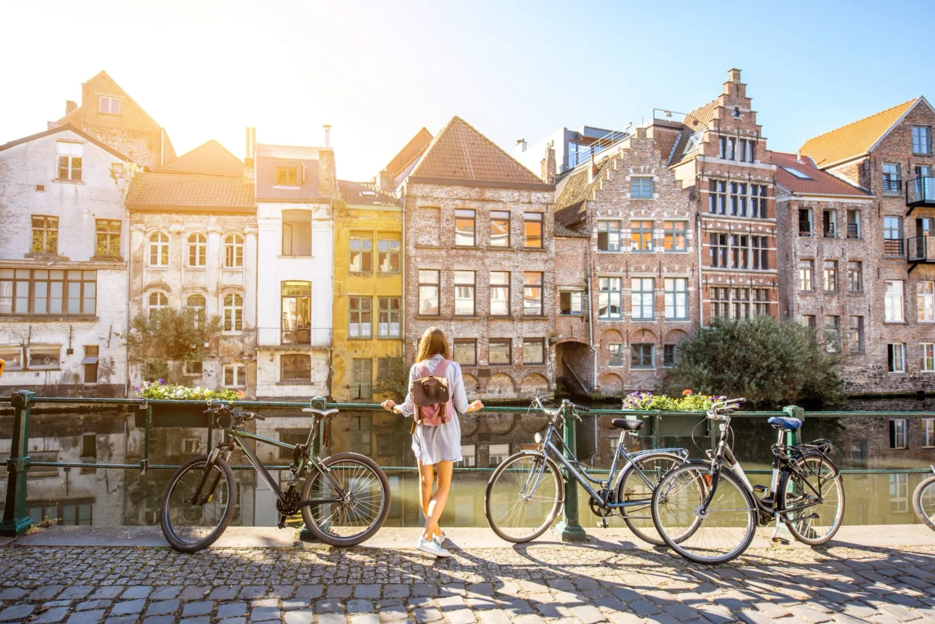 Woman with bicycles near water channel with old buildings in Ghent city.